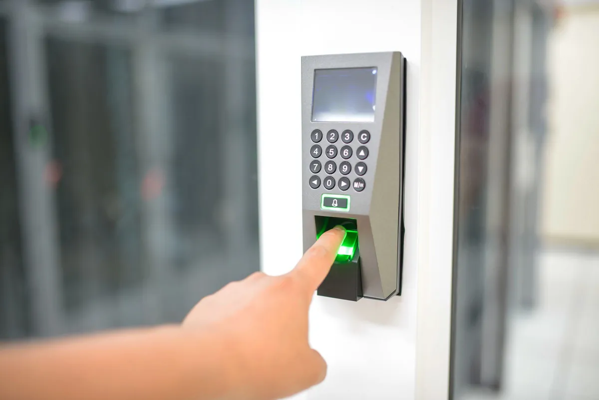 Finger placed on a biometric fingerprint reader with keypad at a door entry point