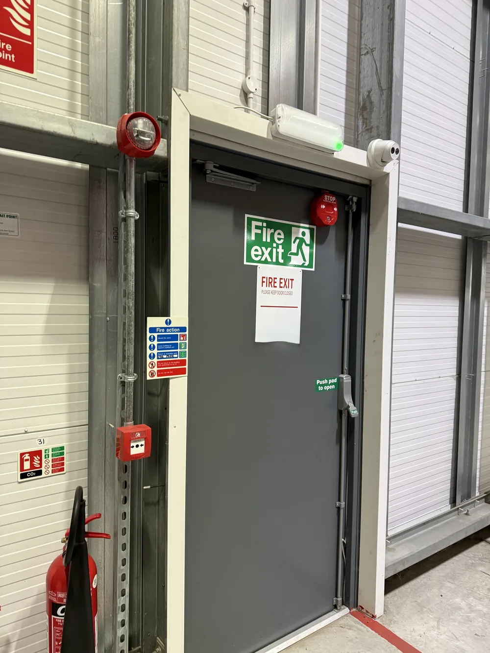 Fire exit in a commercial building with call point, sounder, emergency lighting and extinguisher