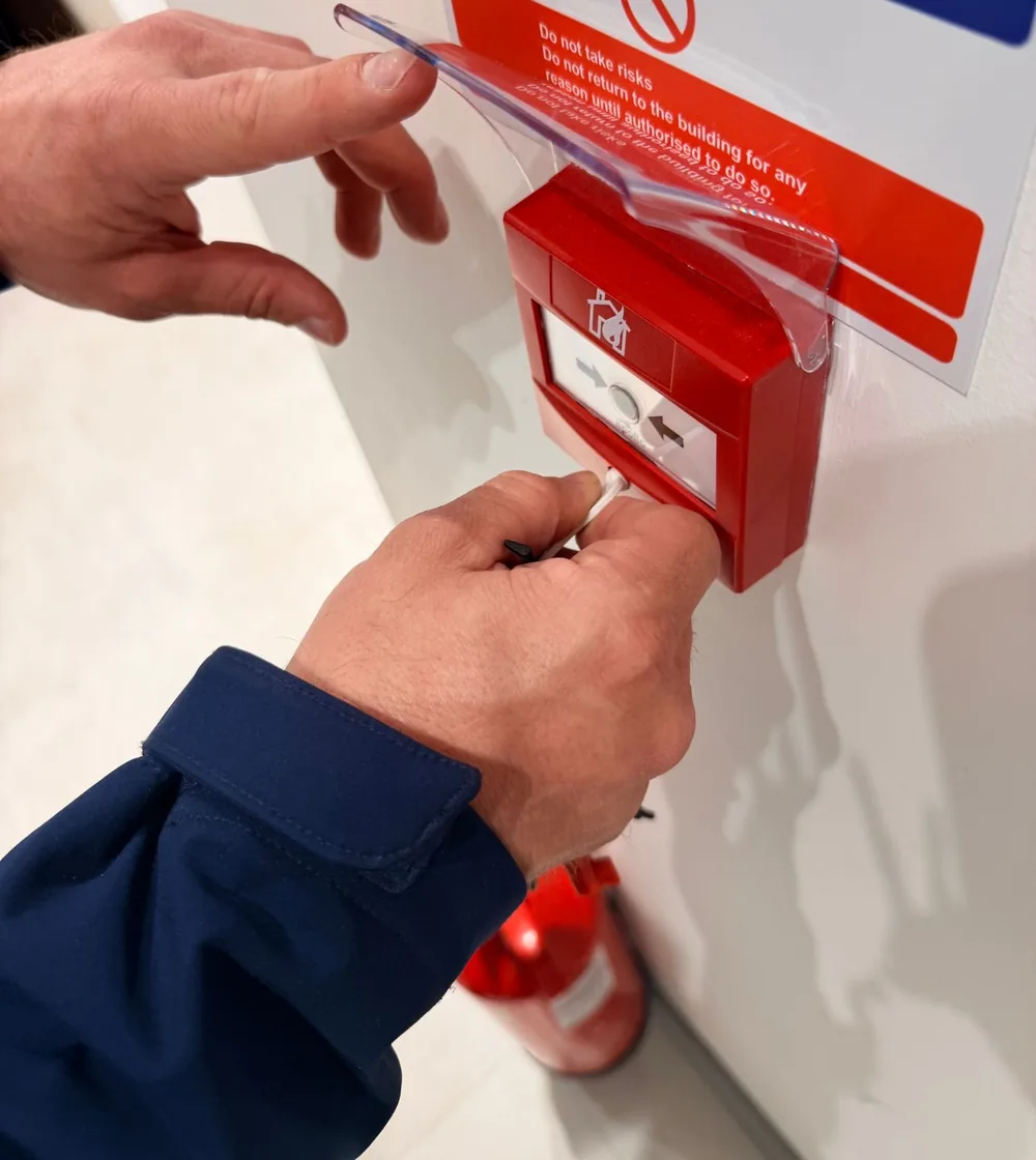 Engineer testing a manual fire alarm call point with a test key