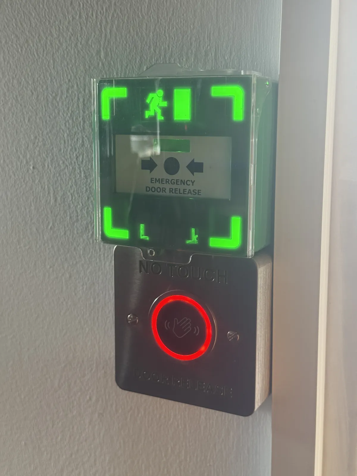 Green emergency door release unit above a no-touch exit button beside an access-controlled door